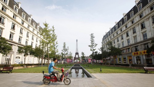 A man rides a motorcycle past a replica of the Eiffel Tower at the Tianducheng development in Hangzhou